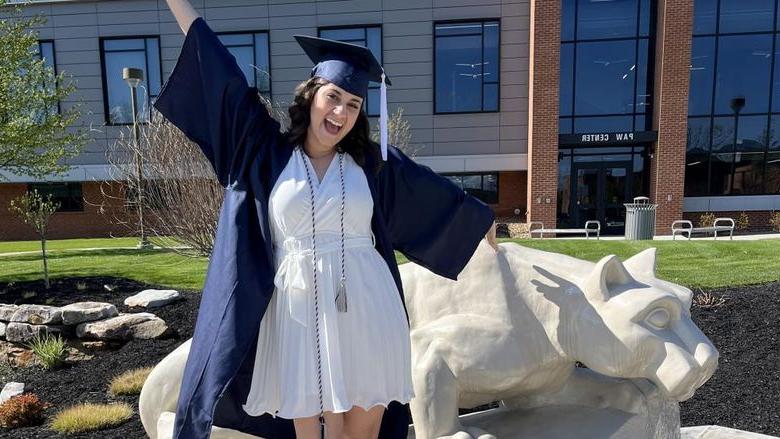 宾州州立大学新毕业生安娜·拉芬纳在宾州州立大学杜波依斯校区的狮子神殿前快乐地庆祝, 就在PAW中心外面